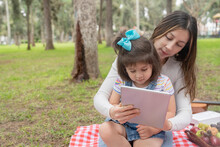 Mother And Daughter Using A Tablet On A Picnic Tablecloth