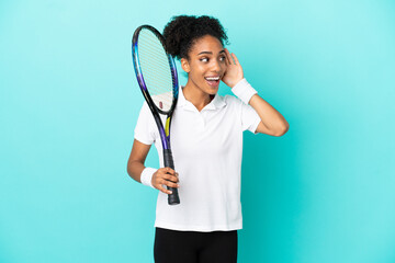 Wall Mural - Young tennis player woman isolated on blue background listening to something by putting hand on the ear