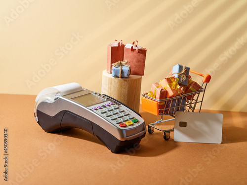Small shopping cart and terminal. Discount card. Beige background. Retail and wholesale, sales, discounts, online shopping. Low angle view.