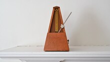 An Old Fashioned Metronome Beating At An Andante Pace On A White Shelf.