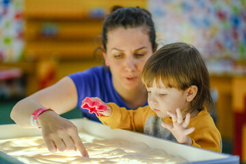 Creative early baby development. A mother teaches her child to draw with her fingers in the sand. Center for the Development of Children with Autism.