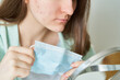 Faceless woman having pimples and blackheads after wearing protective medical mask. Girl looking at mirror and checking pimples on cheek and chin