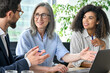 © insta_photos - Happy diverse business people group negotiating business strategy at boardroom meeting table using laptop. Multicultural team discuss project developing financial research working together in office.