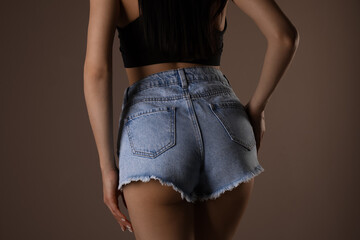 Canvas Print - Slim woman with smooth skin in denim shorts on beige background, closeup. Cellulite problem concept