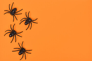 Wall Mural - Plastic spiders on side of bright orange Halloween background with empty copy space