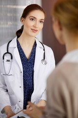 Friendly smiling female doctor and patient woman discussing current health examination in sunny clinic. Perfect medical service in hospital. Medicine concept