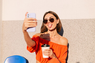 Wall Mural - Stylish woman in orange clothes at sunset at cycle track stadium with cup of coffee and mobile phone take photo selfie