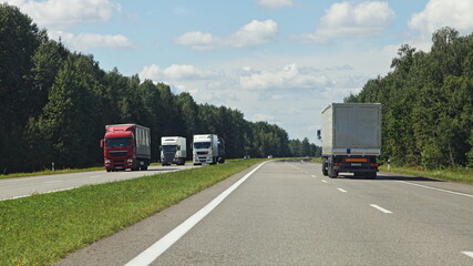 Wall Mural - Two European semi trucks on suburban highway with grassy safety lane at Sunny summer day on blue cloudy sky background, beautiful road landscape