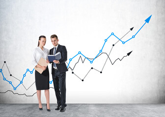 Handsome businessman and attractive businesswoman in formal wear chatting and looking into a book, concrete wall on background. Mockup. Concept of success in career.