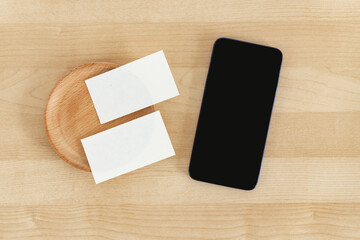 Blank business cards and smart phone on wooden office table. Business card and cell phone Mock Up.