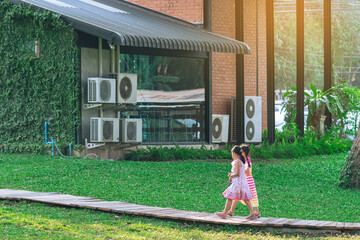 Wall Mural - Asian young girls in dress walking side by side on pathway through green garden.Two girl friends walking together in park. Happy friends spending time together outside in green nature.