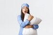 Shocked and concerned young asian girl in sleeping mask and pyjama, hugging pillow and looking tensed as watching intense movie scene, standing white background overwhelmed