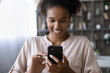 © fizkes - Close up of happy African American woman look at cellphone screen message text online. Smiling young ethnic female use smartphone talk speak on video webcam call on device. Technology concept.