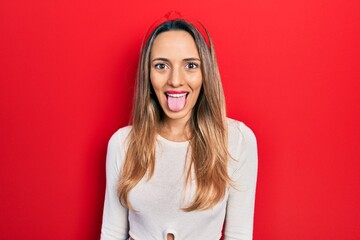 Beautiful hispanic woman wearing red diadem sticking tongue out happy with funny expression. emotion concept.