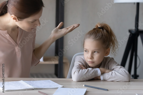 Unhappy young Caucasian mom scold little lazy unmotivated teen daughter studying at home. Upset mother lecture ill-behaved naughty small girl child lack motivation learning. Education problem concept.