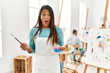 Canvas Print - Young latin woman standing at art studio scared and amazed with open mouth for surprise, disbelief face