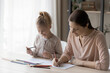 © fizkes - Happy loving young Caucasian mother and small teen daughter sit at desk draw paint together in album. Smiling caring mom and little girl child enjoy artistic activity relaxing. Art, hobby concept.