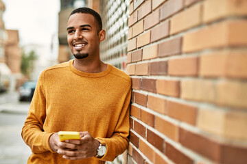 Wall Mural - Young african american man smiling happy using smartphone at the city.