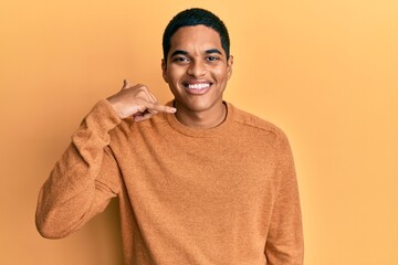 Young handsome hispanic man wearing casual winter sweater smiling doing phone gesture with hand and fingers like talking on the telephone. communicating concepts.