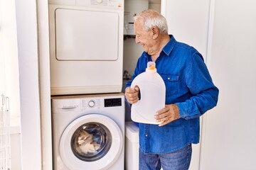 Wall Mural - Senior caucasian man smiling happy holding detergent standing by washing machine at the terrace.