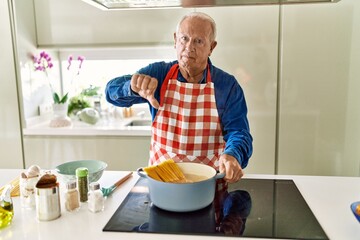 Poster - Senior man with grey hair cooking spaghetti at home kitchen with angry face, negative sign showing dislike with thumbs down, rejection concept