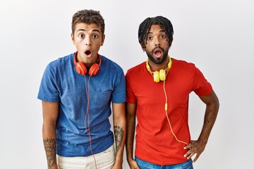 Poster - Young hispanic brothers standing over isolated background wearing headphones afraid and shocked with surprise expression, fear and excited face.