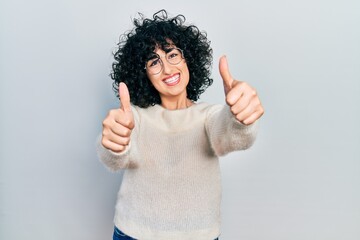 Sticker - Young middle east woman wearing casual white tshirt approving doing positive gesture with hand, thumbs up smiling and happy for success. winner gesture.