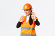 Displeased and reluctant asian female architect in safety helmet grimacing from aversion, showing stop gesture, refuse or rejecting awful disgusting plan, standing disappointed white background