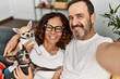 © Krakenimages.com - Middle age hispanic couple smiling happy making selfie by the camera. Sitting on the sofa with dogs at home.