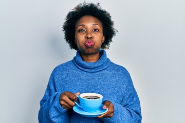 Wall Mural - Young african american woman drinking a cup of coffee puffing cheeks with funny face. mouth inflated with air, catching air.