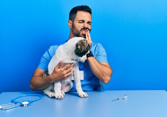 Canvas Print - Handsome hispanic veterinary man with beard checking dog health touching mouth with hand with painful expression because of toothache or dental illness on teeth. dentist concept.