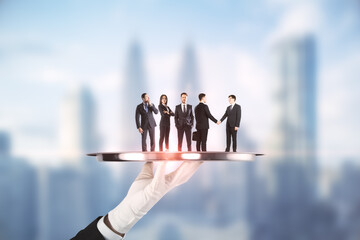 Poster - Hand holding silver tray with businesspeople on abstract blurry city background. Teamwork and service concept.