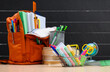 Full shopping basket with stationery on the background of a school backpack and other items. Selective focus on shopping cart.