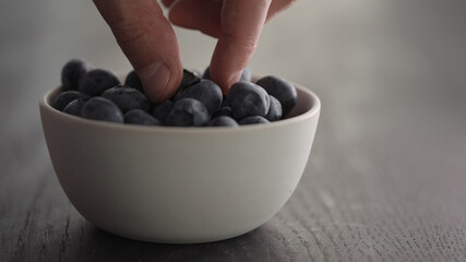 Wall Mural - Man hand pick ripe blueberries from white bowl on oak table