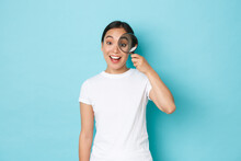 Cheerful Smiling Beautiful Asian Girl Searching For Someone, Hiring To Company, Looking Through Magnifying Glass With Amused Upbeat Expression, Standing Over Light Blue Background