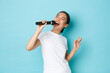 Lifestyle, people and leisure concept. Passionate and carefree pretty asian girl singing song in microphone, bending during performance, like going karaoke, standing light blue background performing