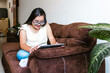 © Marcos - Hispanic teen girl with down syndrome using a tablet while sitting on the sofa at home, in disability concept in Latin America