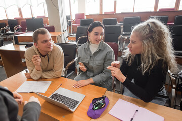 Wall Mural - Two girls and a guy are talking in sign language. Three deaf students chatting in a university classroom.