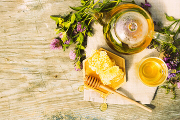 Wall Mural - Tea with fresh leaves of summer herbs clover natural liquid honeycomb in glass teapot cup on a rustic wooden background