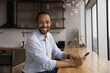 © fizkes - Successful happy African guy holds smartphone smiles looks at camera. Mixed race guy spend time sit in modern home or office kitchen. New mobile professional app usage, lifestyle, e-business concept