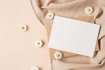 Wall Mural - Blank paper sheet card with mockup copy space, chamomile flower buds and muslin cloth on neutral beige background. Minimal aesthetic wedding invitation template. Flat lay, top view