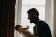 © Ananass - Silhouette of a stylish bearded father kisses a sleeping newborn girl. Parent holding rocking child daughter son in hands. Authentic lifestyle parenting fatherhood moment. Single dad family home life.
