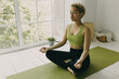 © shurkin_son - Hispanic young woman finding peace in meditation. Girl sitting in yoga position on green mat. Simple, minimalistic interior in room. Yoga, meditation, peace of mind, total relax concept. Copy space