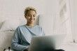 © shurkin_son - Dark skinned teenage girl took sit on floor near white sofa at home in blue pajama watching romantic comedy on laptop, laughing, looking happy, enjoying her leisure time, floor mirror on background