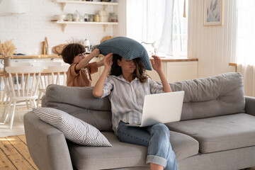 Wall Mural - Annoyed irritated female try to work from home with hyperactive preschool kid. Naughty small child hit mother with pillow. Mom and son on covid quarantine. Freelance occupation and parent lifestyle