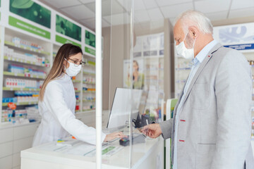 Wall Mural - Shopping prescription drugs and pharmacist's advice, prescription drugs. A side view of a pharmacist standing behind a counter selling medicine to an mature man wearing a protective mask