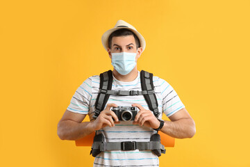 Sticker - Male tourist in protective mask with travel backpack and camera on yellow background