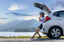 Young Asian Woman Traveler Sitting On Hatchback Car Trunk With Mountain Landscape Background. Traveler Car Concept