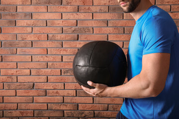 Canvas Print - Athletic man with medicine ball near red brick wall, closeup. Space for text