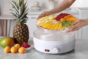 Poster - Woman putting tray with cut fruits into dehydrator machine at grey marble table in kitchen, closeup